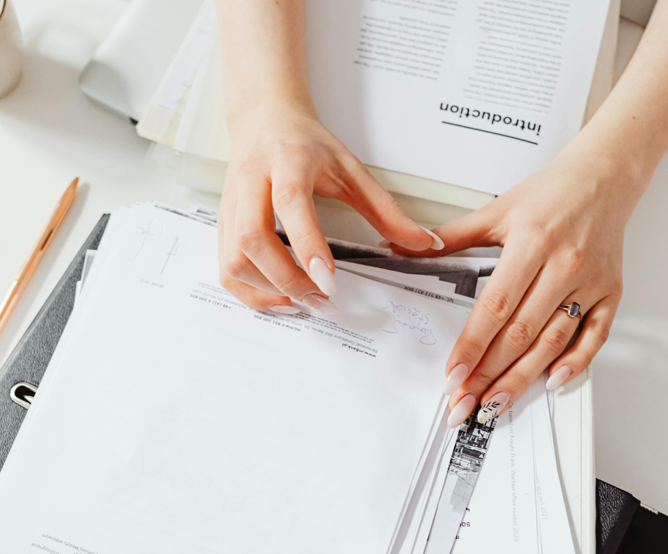 Close-up of a woman's hands managing paperwork on a desk, showcasing organization skills.