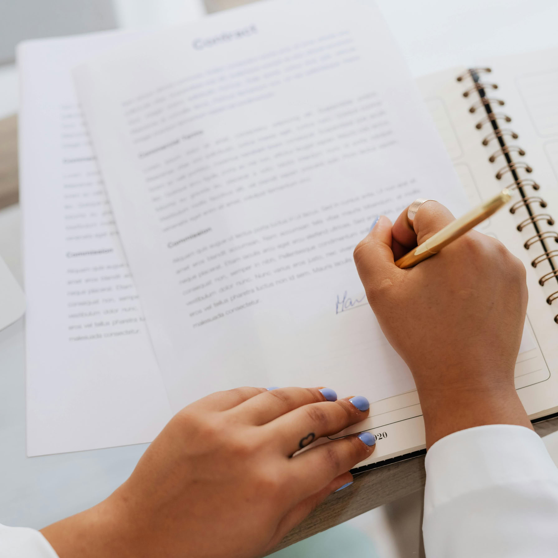 Woman signing a contract with a gold pen, focus on hands and document.