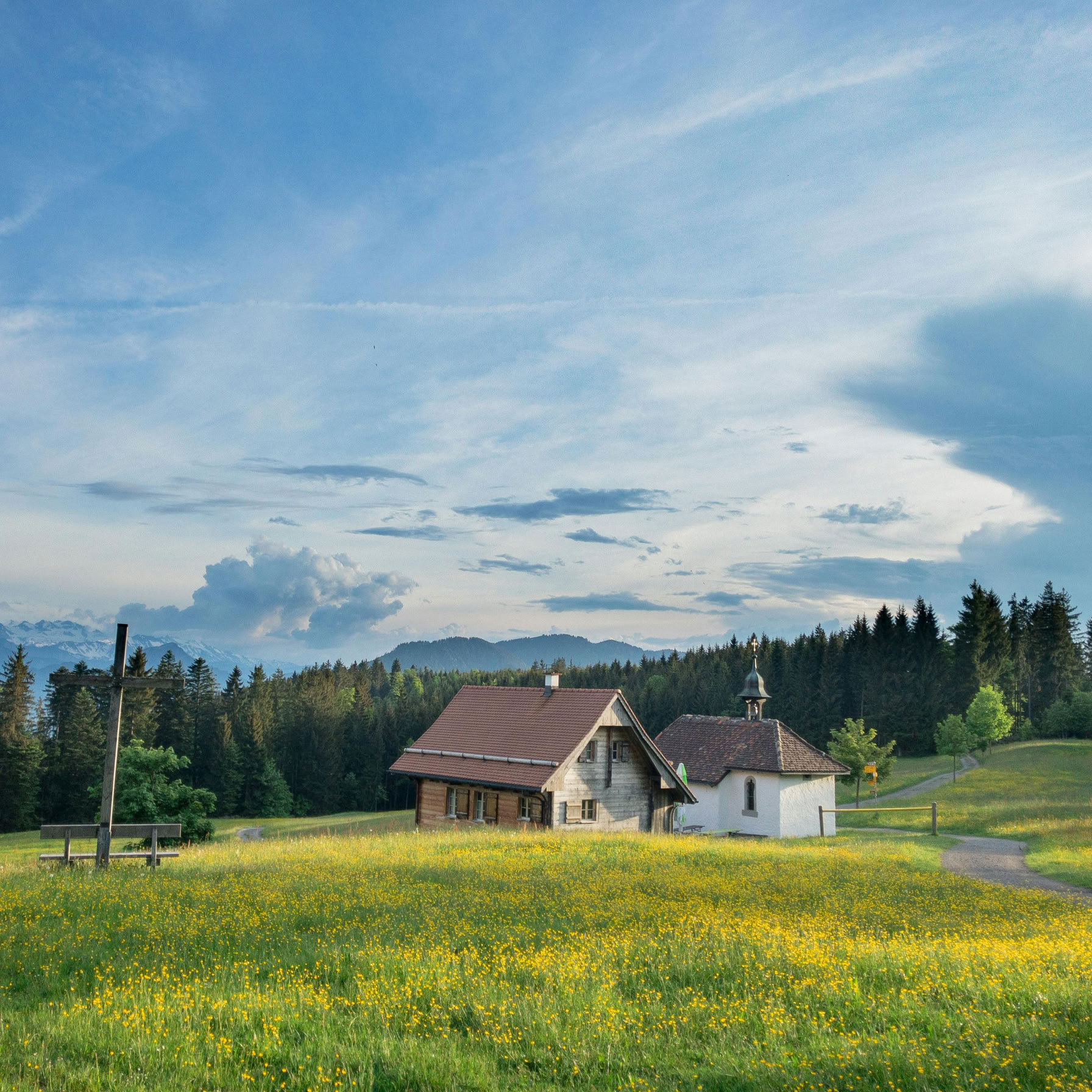 Charming Swiss countryside scene featuring a farmhouse and chapel amidst lush green fields and forests.