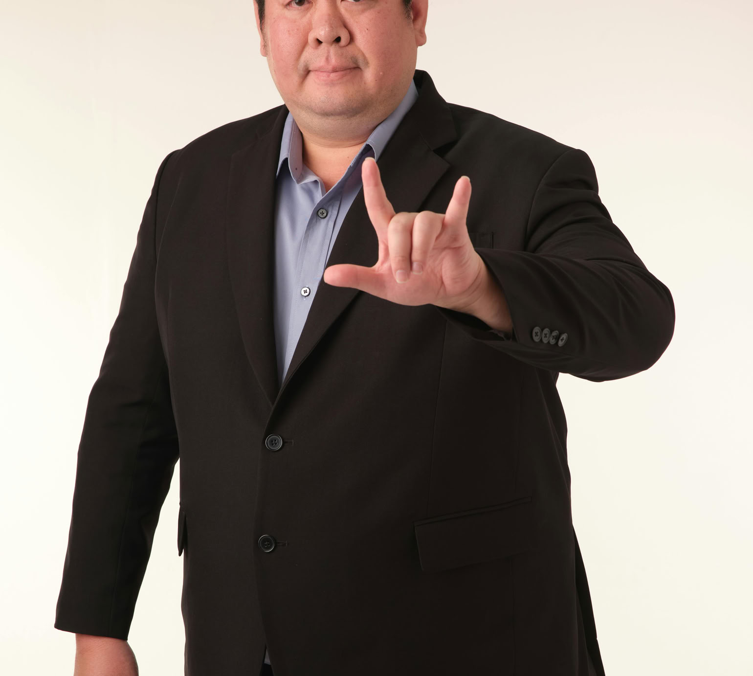 A confident adult man in a suit gestures 'I love you' in sign language.