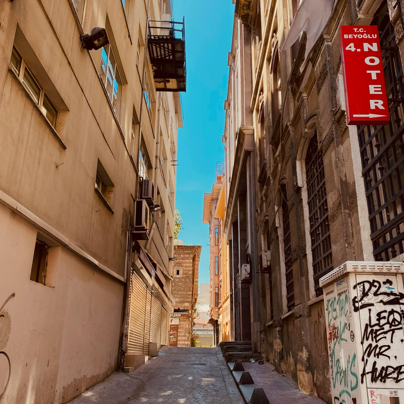 Narrow cobblestone alley in Beyoğlu between buildings with a clear blue sky.