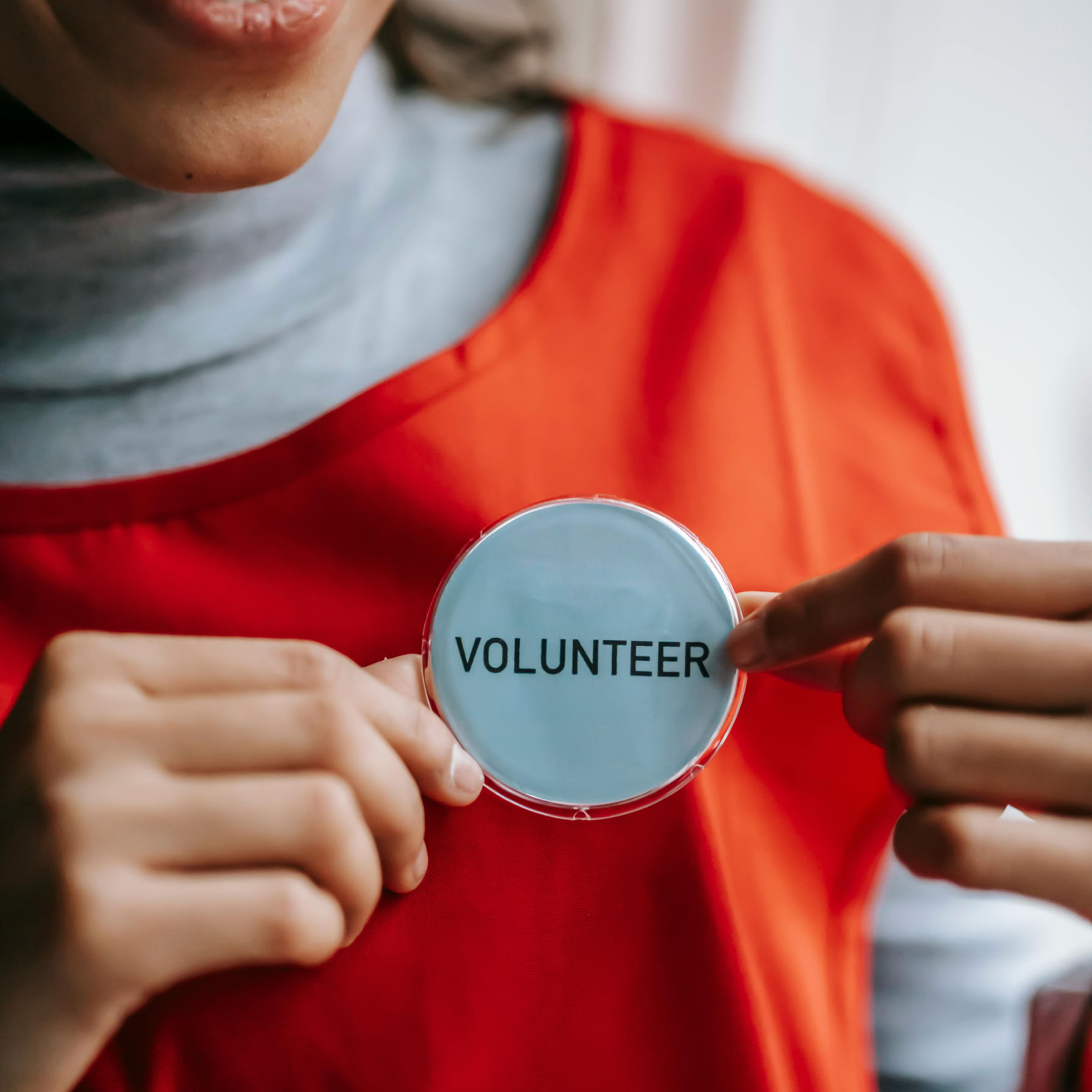 Close-up of a smiling volunteer holding a badge in a bright setting.